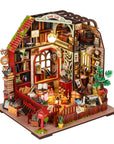 A miniature book-lift dollhouse model with intricate interior details, including bookshelves, a desk, plants, and warm glowing lights, shown on a plain white background.