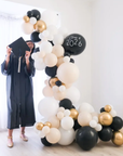 balloon garland with a graduate standing next to it, in balck, white, cream and gold colors