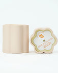 Light peach container of a candle's side view and top view. Top view has paper cover of scent and text