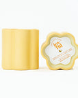 Yellow container of a candle's side view and top view. Top view has paper cover of scent and text