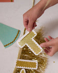 Child's hands holding a gold glittery number one cutout with colorful paper triangles in the background.