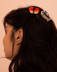 Person with hair styled with colorful hair clips against a pink background