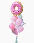 A pink donut-shaped foil balloon with sprinkles and a smiling face, arranged together with latex balloons in pink and lavender, a translucent confetti balloon, a lavender star balloon, a pink heart balloon, and a tassel.