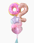 A cluster of birthday balloons on a white background, featuring a pink donut balloon with a smiling face, a metallic rose gold number 2 balloon, a lavender star balloon, and pink heart balloons with confetti.