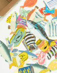 Colorful fish-shaped stickers on a white surface with a cardboard box in the background.