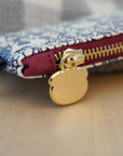 A close up zipper view of the multicolored coin purse with a brass zipper and a metal key ring, featuring a pattern of guinea pigs, flowers, and leaves with a blurred background