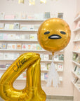A gold balloon with a gudetama face and part of a number 4 balloon