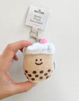 A plush keychain designed to look like a boba tea drink with a smiling face, brown sugar dots, and a blue straw on top.