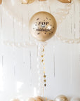 Decorative balloon with 'Pop at midnight!' text hanging among other balloons against a white wooden background.