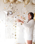 Woman in a white dress celebrating with balloons and confetti in a festive setting.