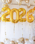 NYE BALLOONS 2026 in gold with gold and white balloons floating above in the ceiling and on the floor.