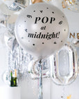 A silver round balloon filled with text "Pop at Midnight" in front of festive background