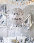 A silver round balloon filled with text "Pop at Midnight" in front of festive background