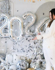 A girl wearing white with confetti flying everywhere from the popped balloon