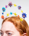 Colorful star-shaped headband worn by a person with red hair on a light gray background
