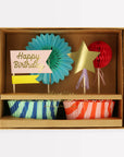 Colorful birthday party supplies including paper fans, a star, and striped cups in a box.