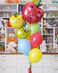A set of colorful balloons designed to look like apples with the name 'Luca' and the grade '1st Grade' printed on them, along with a handmade tassel.