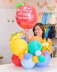 a woman holding an apple balloon with a tabletop balloon gift