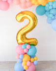 A rainbow number balloon stack with a gold 2 sitting on top