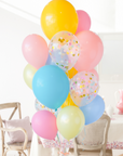 A bouquet of balloons in shades of blue, pink, yellow, and multicolor with a confetti pattern. Bouquet is in a dining room setting.