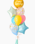 A balloon bouquet featuring a round gold orb balloon, with smaller multicolored balloons including pink, blue, and yellow, all adorned with confetti clear balloons and stars. The balloons are attached to a ribbon bow and tassel.