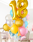 A balloon arrangement featuring a golden number '18' balloon with multicolored balloons tied to it, with the word 'Happy Birthday' printed on a gold balloon. Bouquet is in front of a dining table