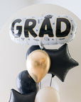 A balloon arrangement with a large 'GRAD' letter balloon in gold and black, surrounded by smaller black balloons.