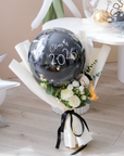 Bouquet with a black balloon featuring 'Class of 2026' text on a wooden floor.
