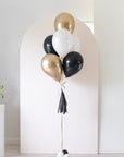 graduation balloon bouquet in black, white, cream and gold colors in front of an arch backdrop