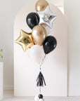 Balloon bouquet with gold, black, and silver star balloons with an arch backdrop