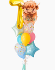 A balloon bouquet featuring a Highland cow balloon with the text 'herd it was your birthday', a gold 7 number balloon and several coordinating balloons including a yellow round balloon, pastel blue and pink balloons, and two light blue star-shaped balloons with confetti.