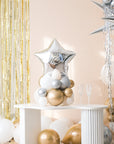 A balloon centerpiece featuring a shiny star-shaped balloon, placed on a white table with gold-colored balloons and star-shaped decorations in the background.
