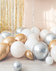 Cream, white, gold and silver balloons on the floor with a gold tinsel curtain and cream backdrop