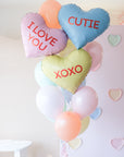 A bunch of heart-shaped balloons in various colors with love-related phrases written on them, such as 'I LOVE YOU' and 'XOXO'.