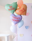 A bunch of heart-shaped balloons in various colors with love-related phrases written on them, such as 'BE MINE' and 'TRUE LOVE' and 'SWEET HEART'