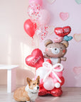 A Valentine's Day balloon present featuring a heart-shaped balloon with the name 'Olivia', a teddy bear holding balloons, and a corgi dog sitting in front.