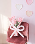 A bouquet of pink balloon roses with a white balloon bow on a pink chair against a pink wall with heart decorations.