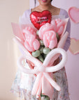 A person holding a bouquet of pink balloon roses, a red balloon heart, and a balloon bow.