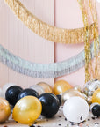 Assorted gold, silver, black, and white balloons scattered on the floor around a pink wall, with some balloons uninflated and others inflated.