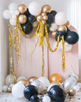 Assorted gold, silver, black, and white balloons scattered on the floor around a pink wall