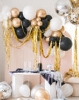 Assorted gold, silver, black, and white balloons scattered on the floor around a pink wall