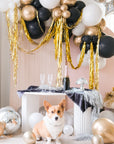 Assorted gold, silver, black, and white balloons scattered on the floor around a pink wall