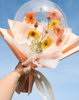A balloon bouquet arrangement with spring poppies faux flowers, wrapped in peach and white materials against a blue sky.
