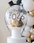 clear balloon with mini balloons inside on top of a white box, with graduation cap and "class of 2026" text 