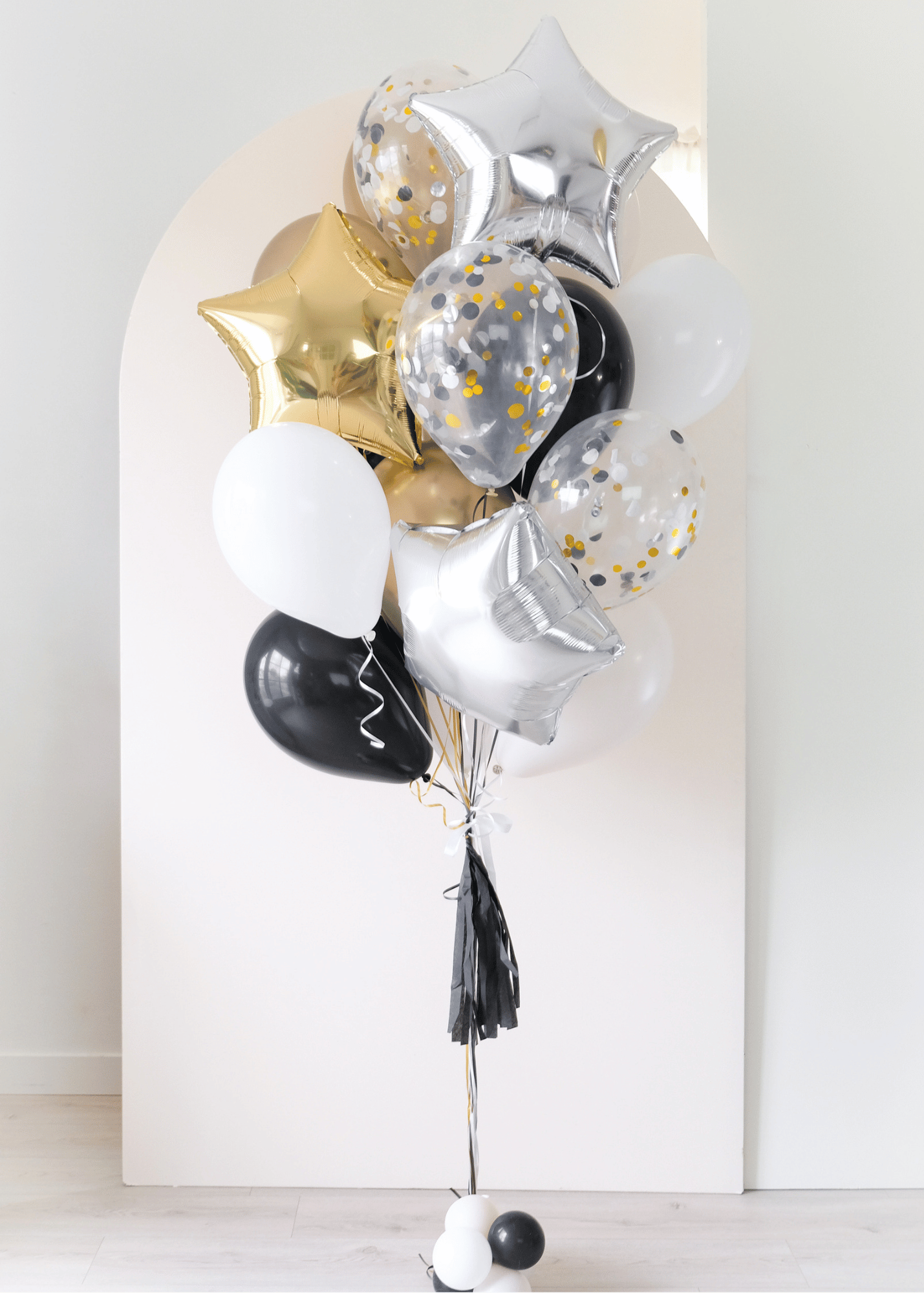 assorted graduation balloons in black, white, gold in front of an arch backdrop