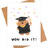 Graduation-themed card with a dog in a cap and gown, holding a diploma, and confetti on a white background.