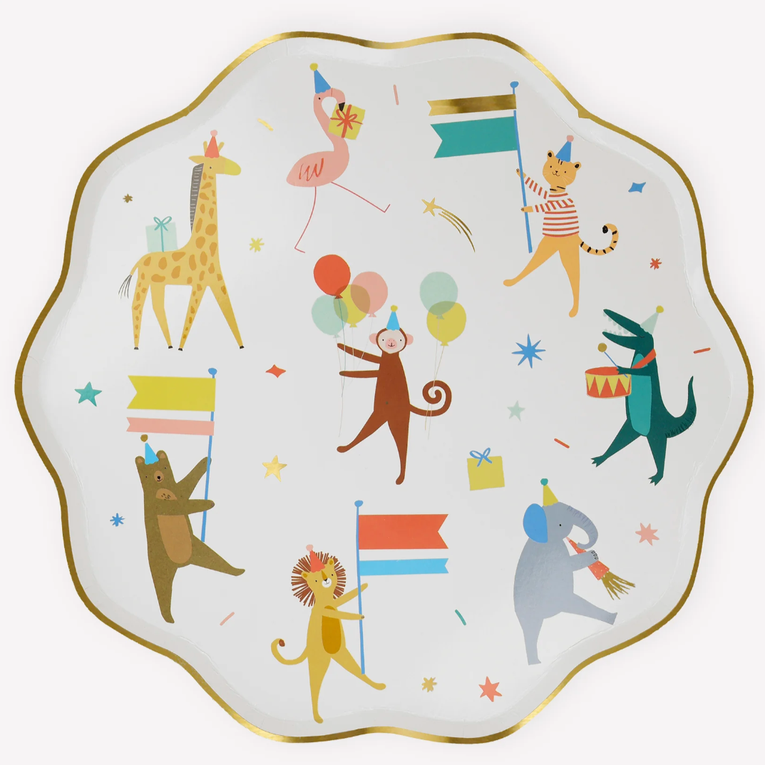 A round white dinner plate with scalloped gold foil border featuring a parade of colorful animal illustrations, such as a giraffe, monkey, and lion, along with party elements like balloons and flags.