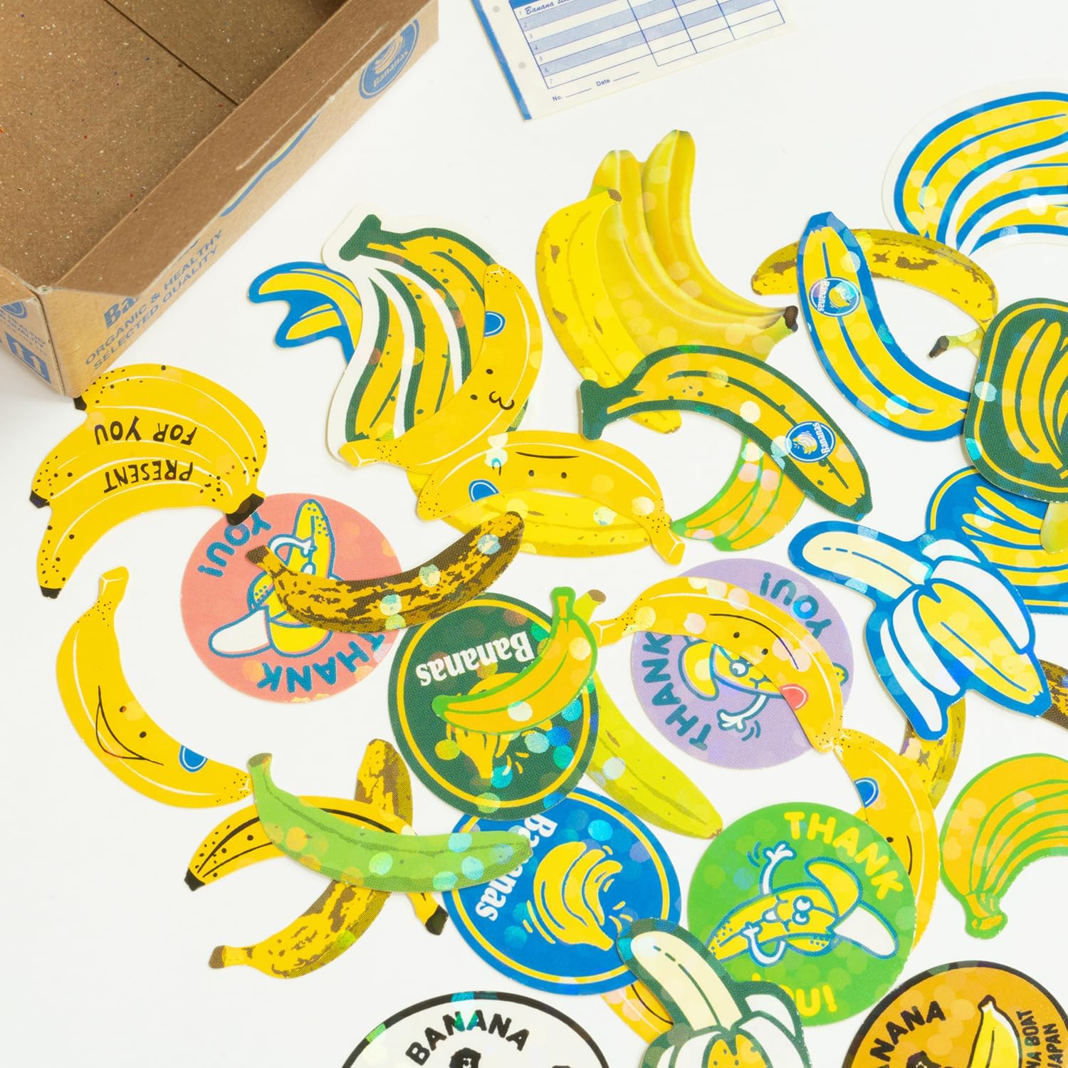 Colorful banana-themed stickers on a white surface with a cardboard box in the background.