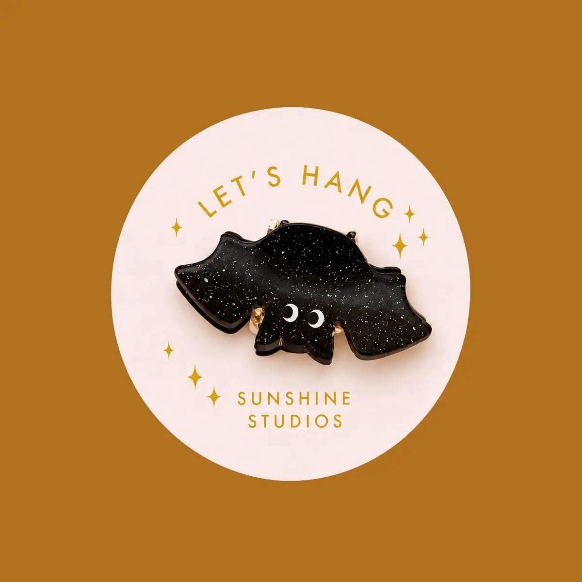 A black glittery bat-shaped hair clip over pink circle packaging