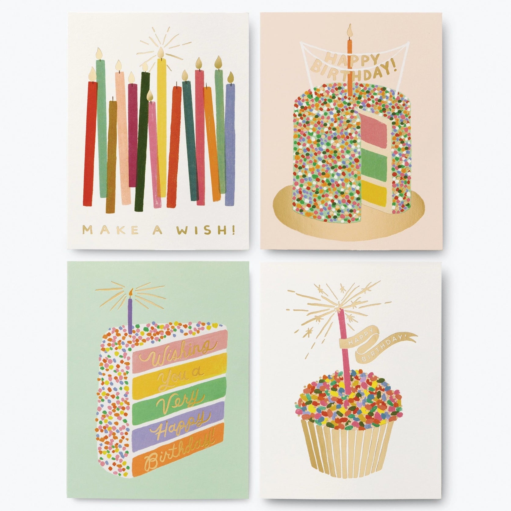 A set of four birthday cards with colorful candle designs, placed outside a paper-wrapped box with gold foil accents.